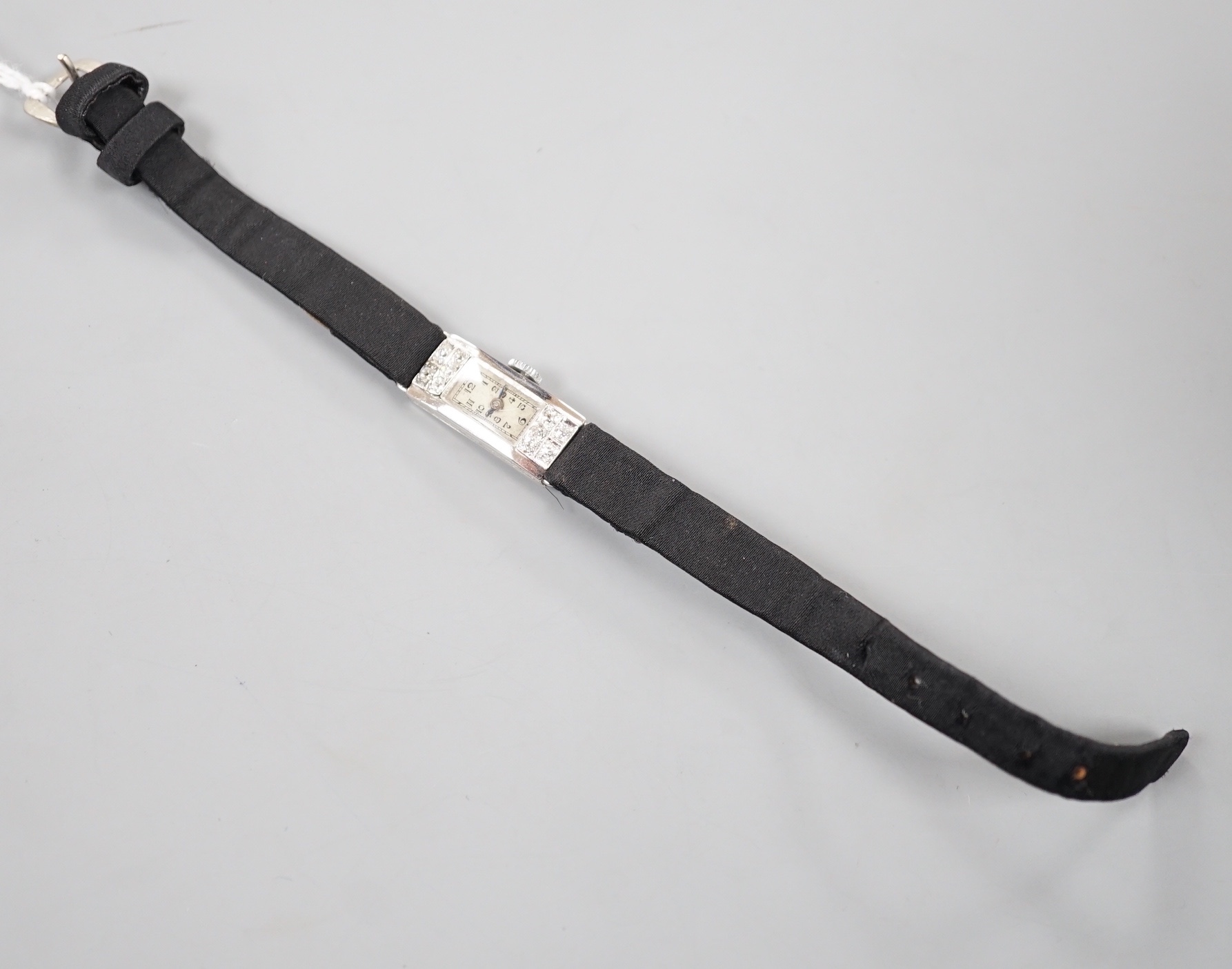 A lady's white meat (stamped Platinum) and diamond set rectangular manual wind cocktail watch, case diameter 11mm, on a black fabric strap, gross weight 10.3 grams.